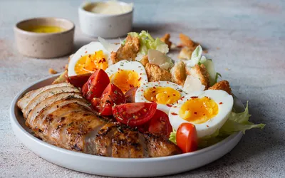 A balanced meal featuring grilled chicken, hard-boiled eggs, and fresh salad.