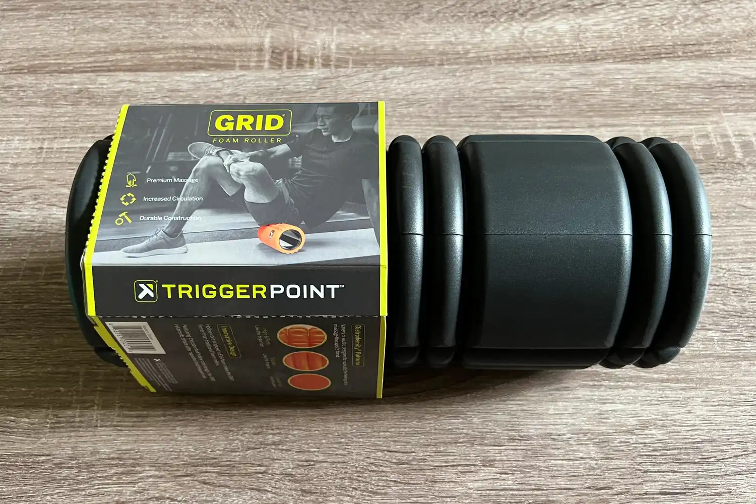 Black TriggerPoint GRID Foam Roller with its retail packaging on a wood surface.