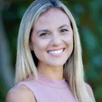 A smiling woman in athletic clothing standing in a natural outdoor environment.