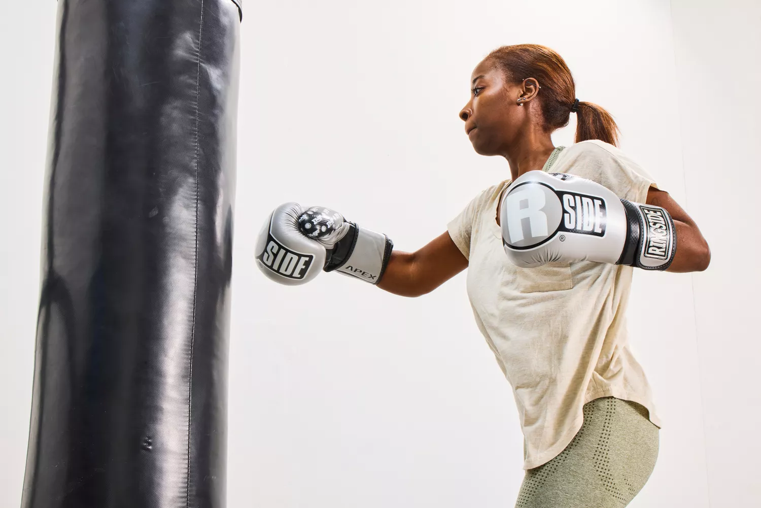 A woman using silver Ringside boxing gloves on a heavy bag in a studio.