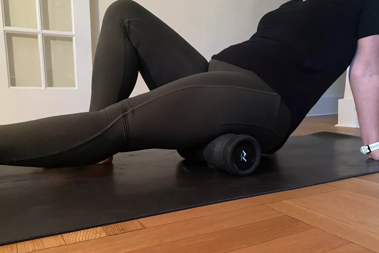 An individual using a textured foam roller on their glutes on a yoga mat.