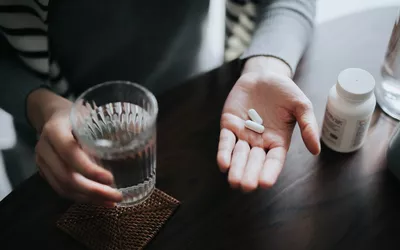 A person holding pills next to a glass of water, representing the medical management or supplement phase of IBS treatment.