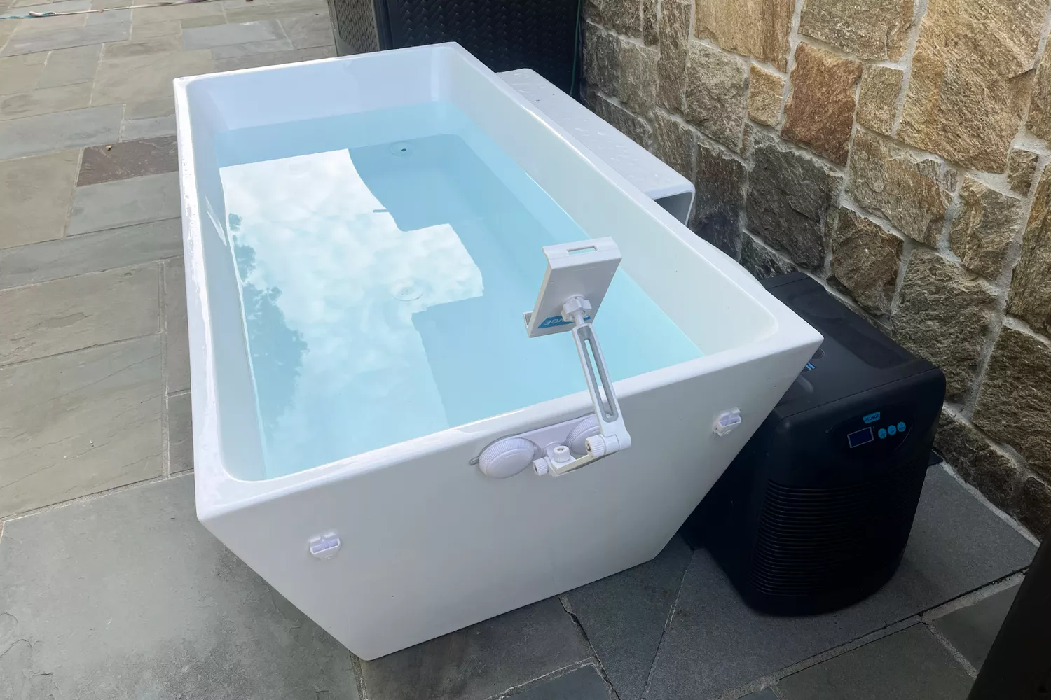 A sleek white Plunge tub setup on a stone patio with a digital temperature display.