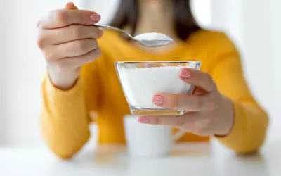 A person holding a spoon over a bowl of sugar, illustrating dietary sugar intake.