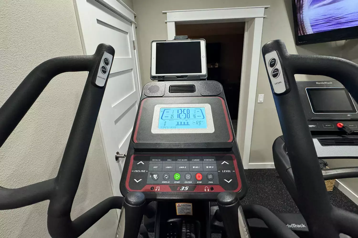 First-person view of a Sole E35 elliptical console with a mounted tablet in a home gym.