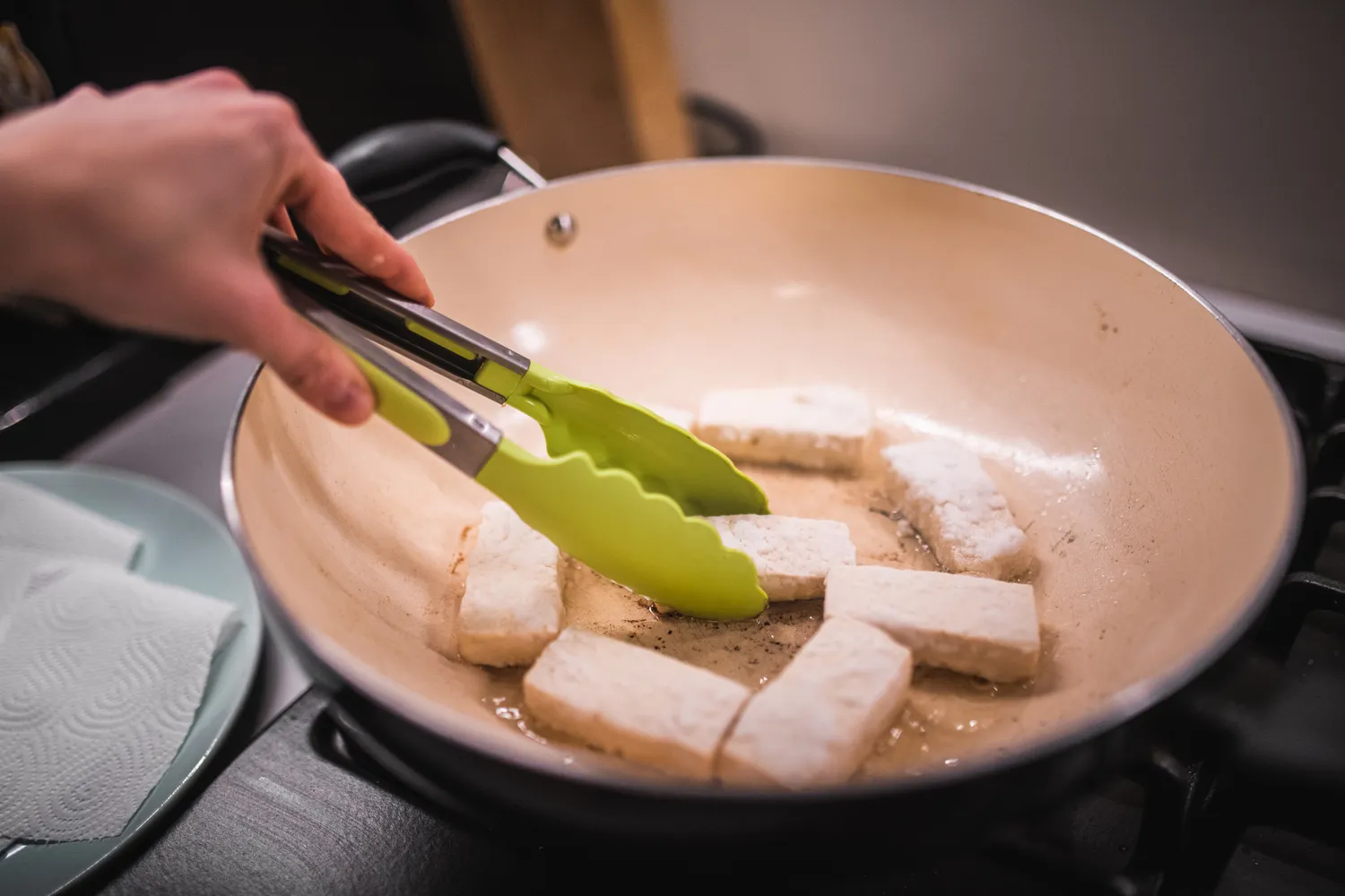 A person cooking sliced tofu in a pan.