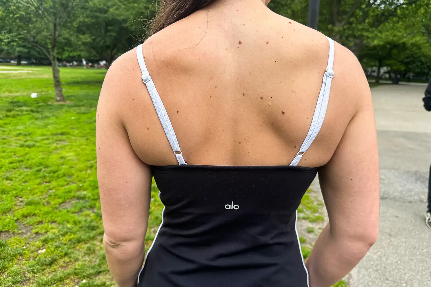 Back view of a woman wearing a black Alo Yoga dress with white straps in a park.