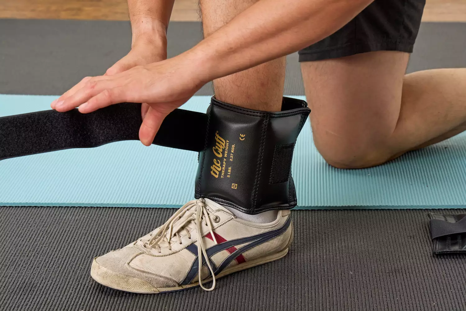 A person securing a 5-pound 'The Cuff' ankle weight with heavy-duty Velcro straps.