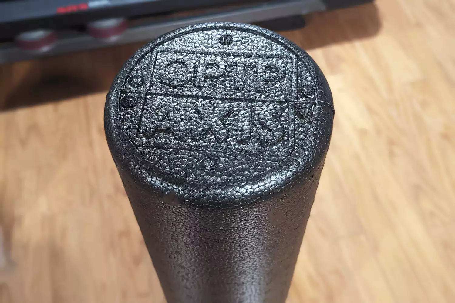Close-up of the textured surface of a black OPTP Axis firm foam roller on a wood floor.
