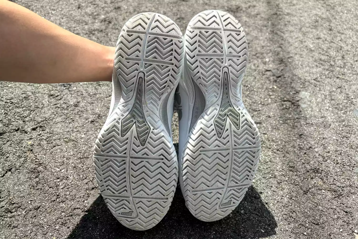 A person holding up athletic sneakers to show the zigzag tread patterns on the sole.