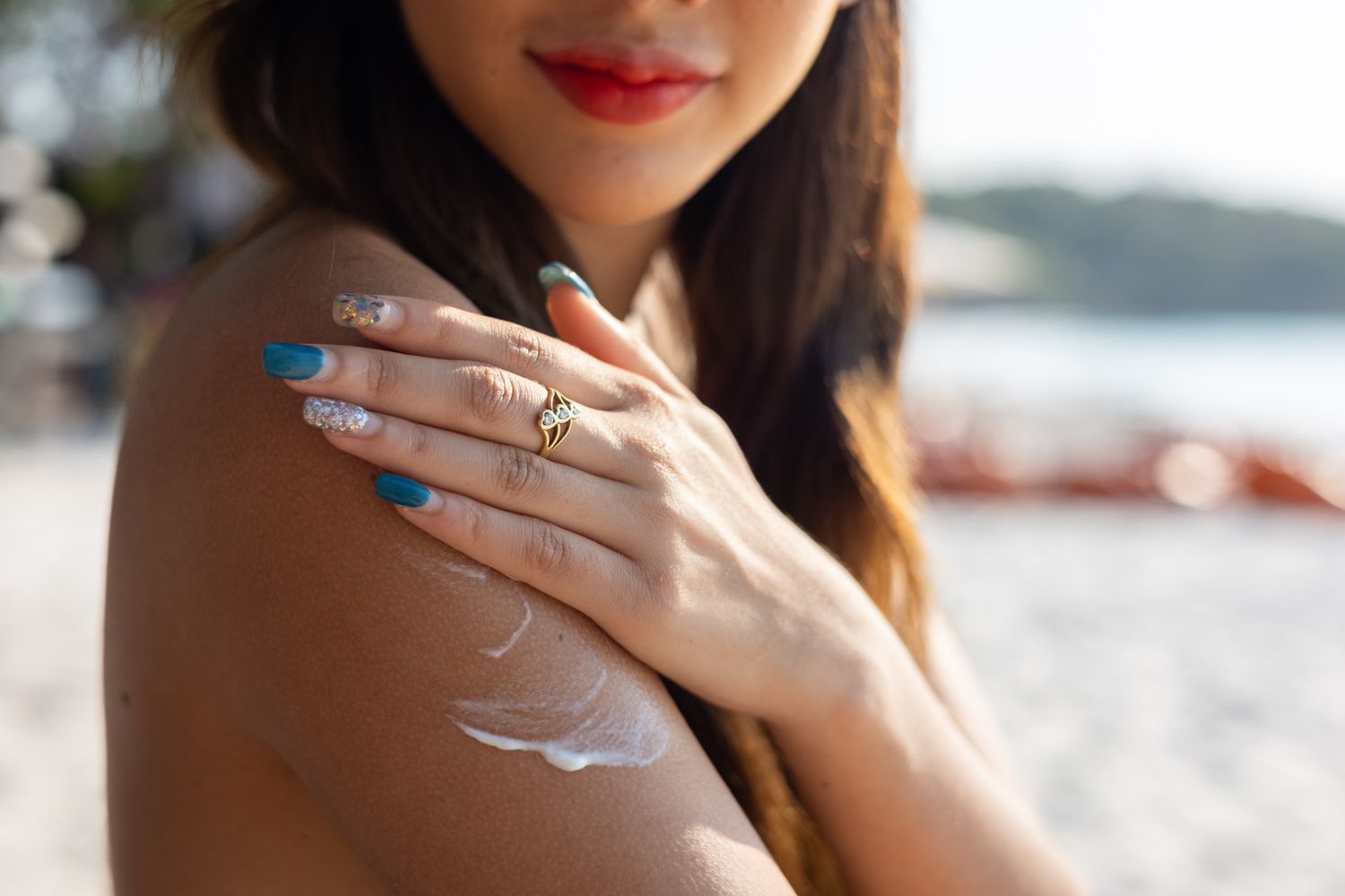 A woman applying sunscreen to her shoulder at the beach.