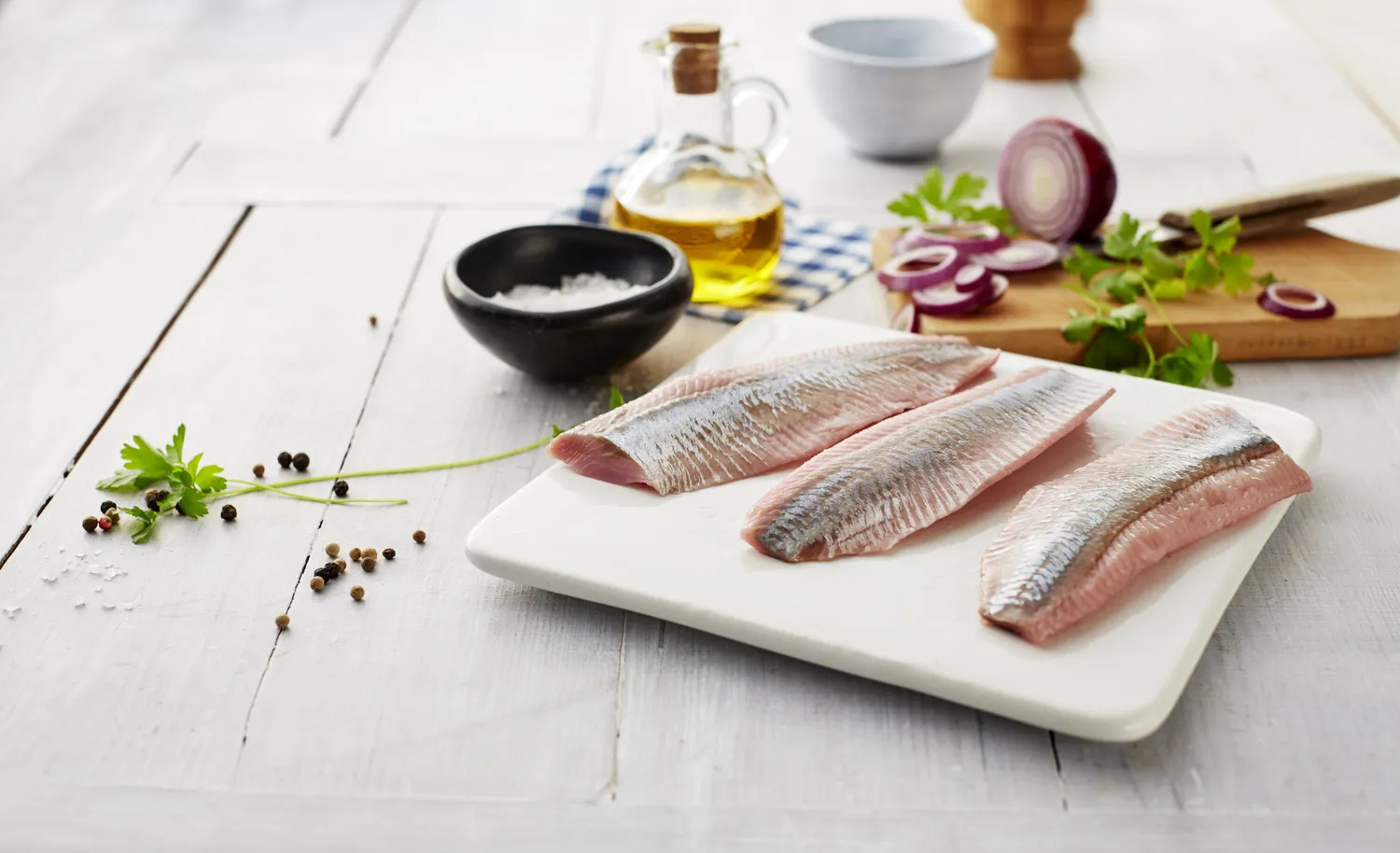 Raw herring fillets on a plate with red onions, herbs, and peppercorns.
