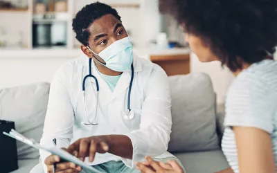 A doctor in a white coat consulting with a patient during a home wellness visit.