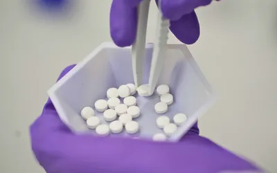 Close-up of pharmaceutical handling of white pills in a laboratory setting.