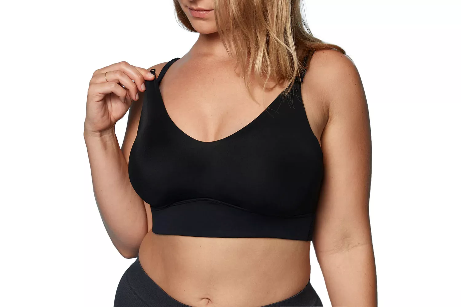 A woman demonstrating the nursing clip and strap adjustment on a black sports bralette.