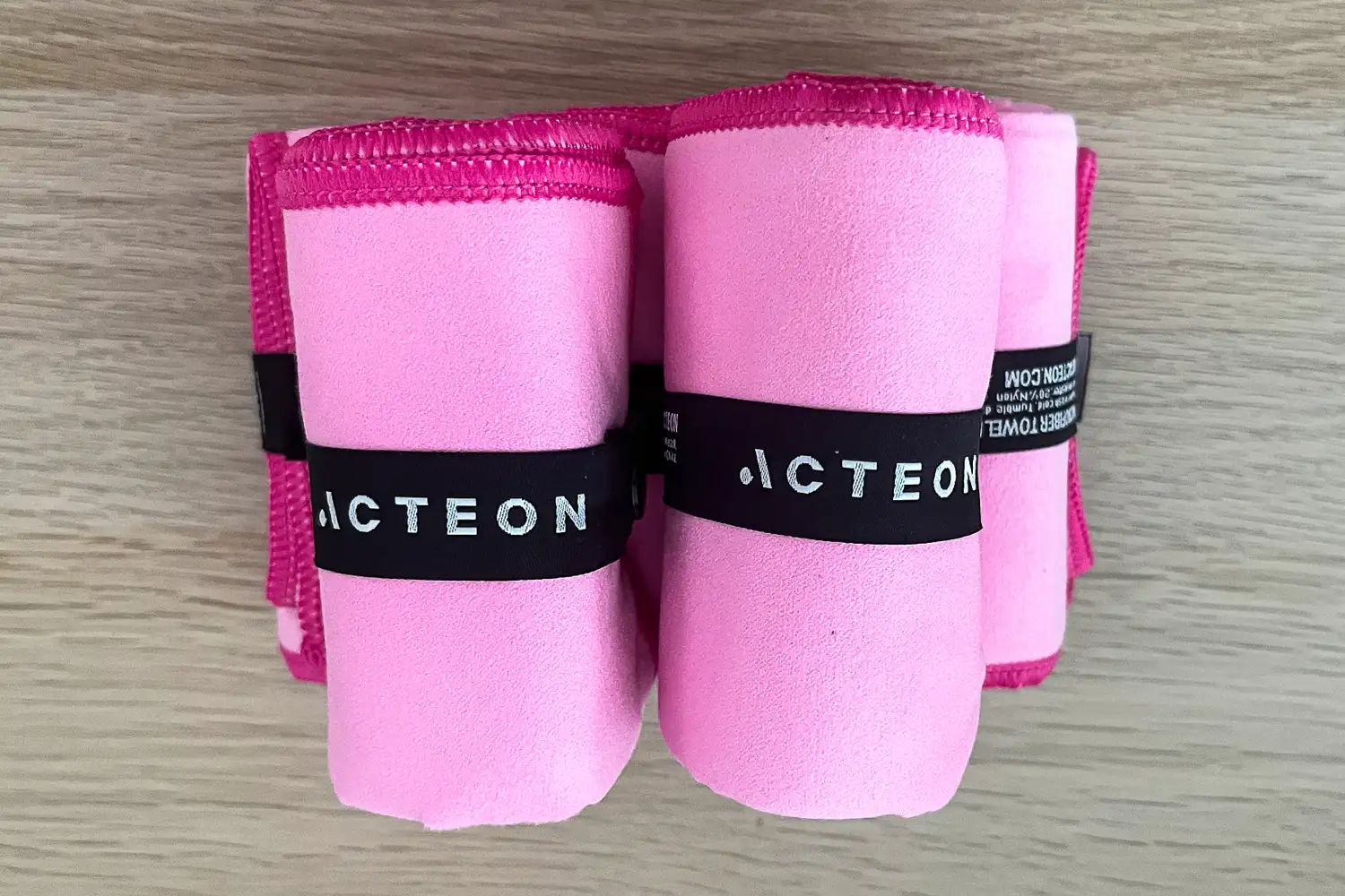 Three pink Acteon microfiber towels rolled up and secured with integrated branded straps.