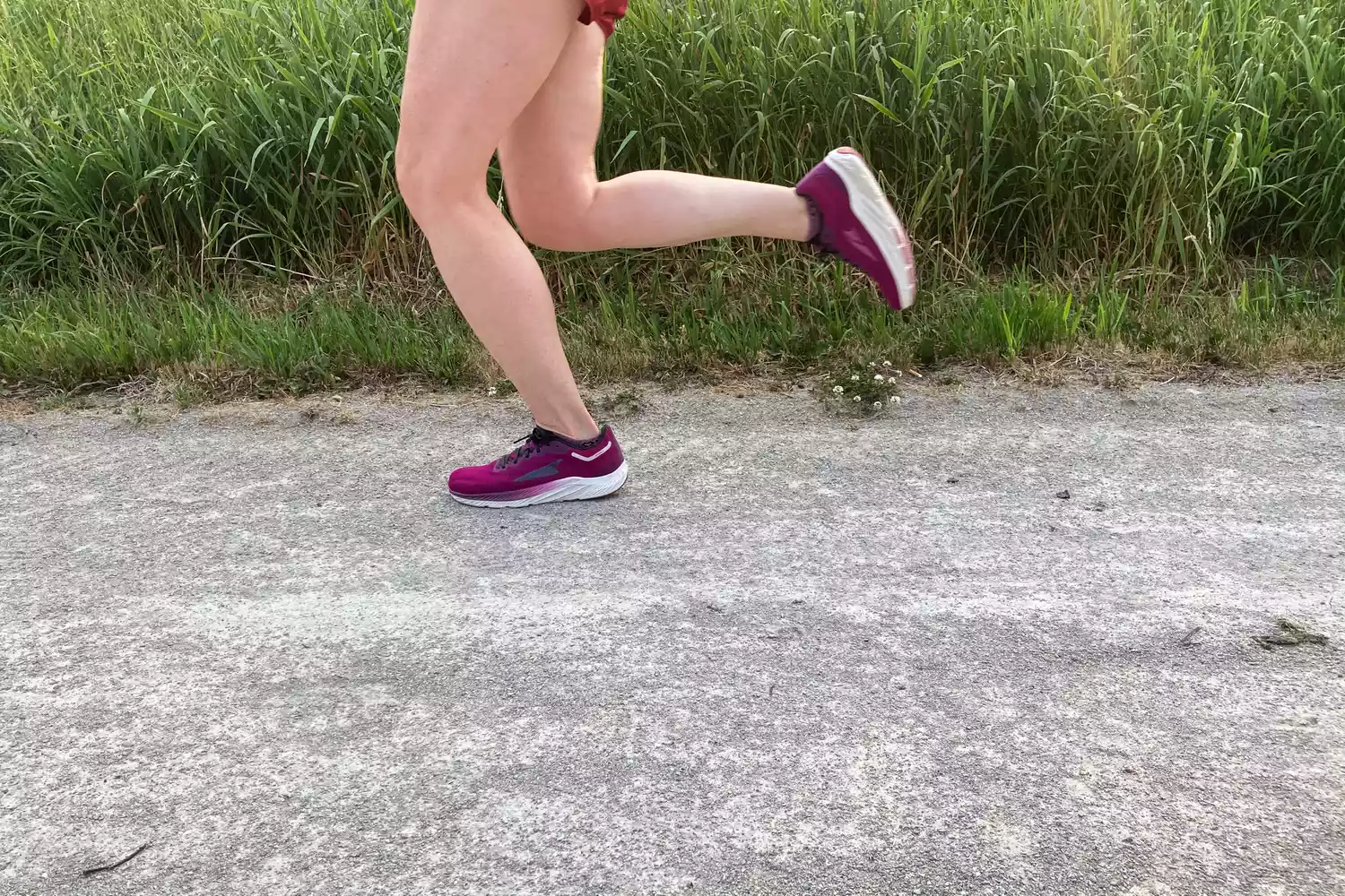A runner wearing purple Altra Rivera 3 shoes mid-stride on a gravel path.