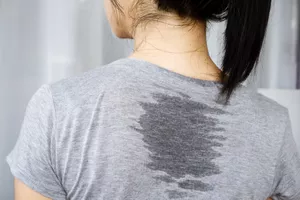 A woman from behind wearing a gray t-shirt with a large sweat stain on her back.