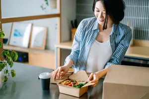 A woman opening a prepared healthy lunch box with vegetables and protein.