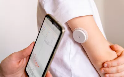 A person checking real-time glucose levels on a smartphone app synced to a CGM on their arm.