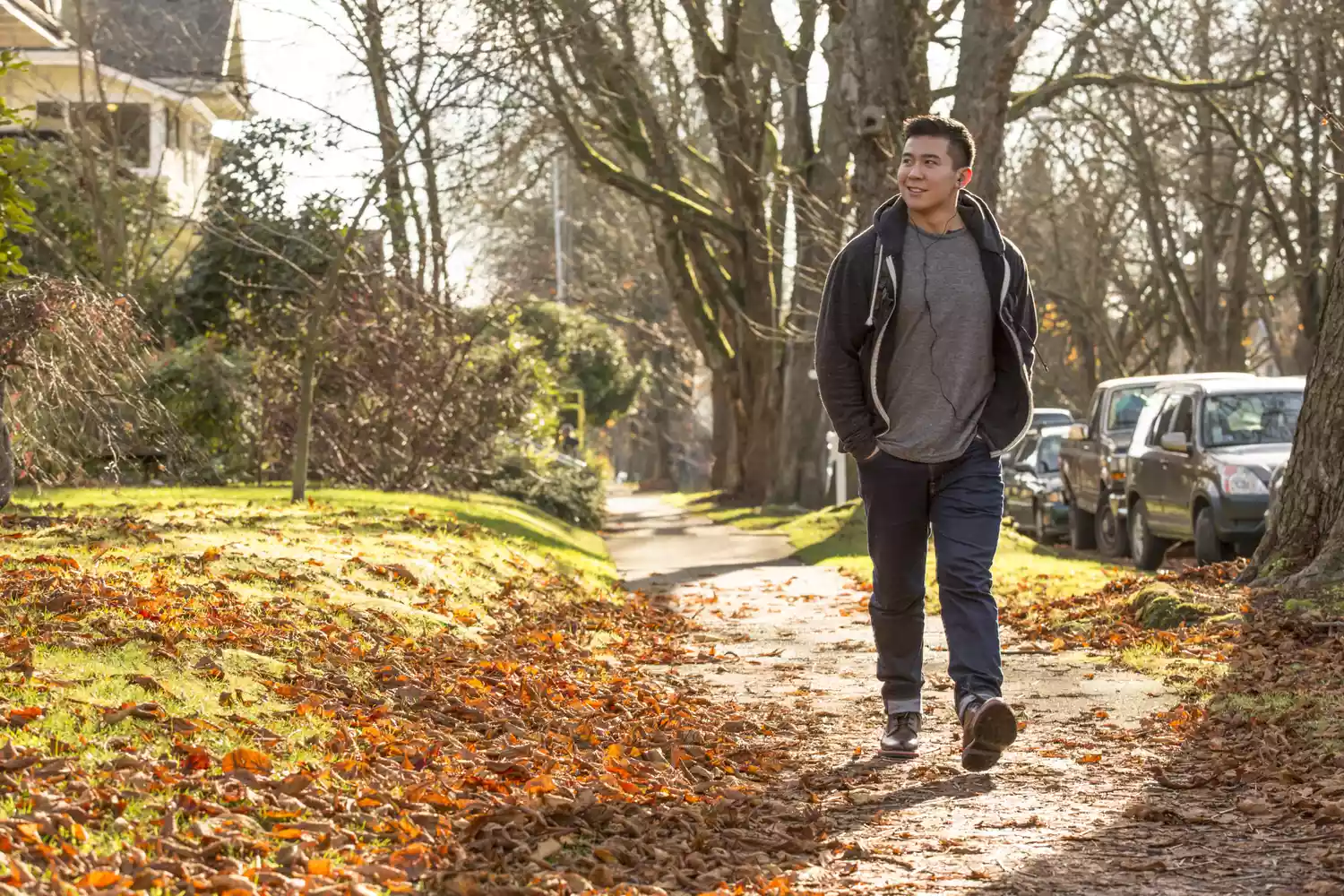 A man walking briskly on a sidewalk lined with autumn trees.