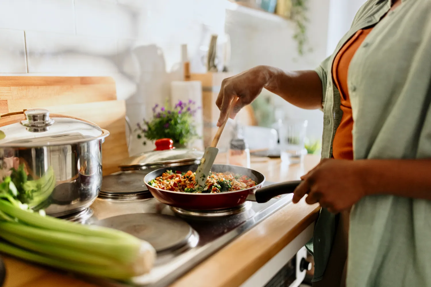 A person cooking a healthy stir-fry with quinoa and fresh vegetables in a skillet.