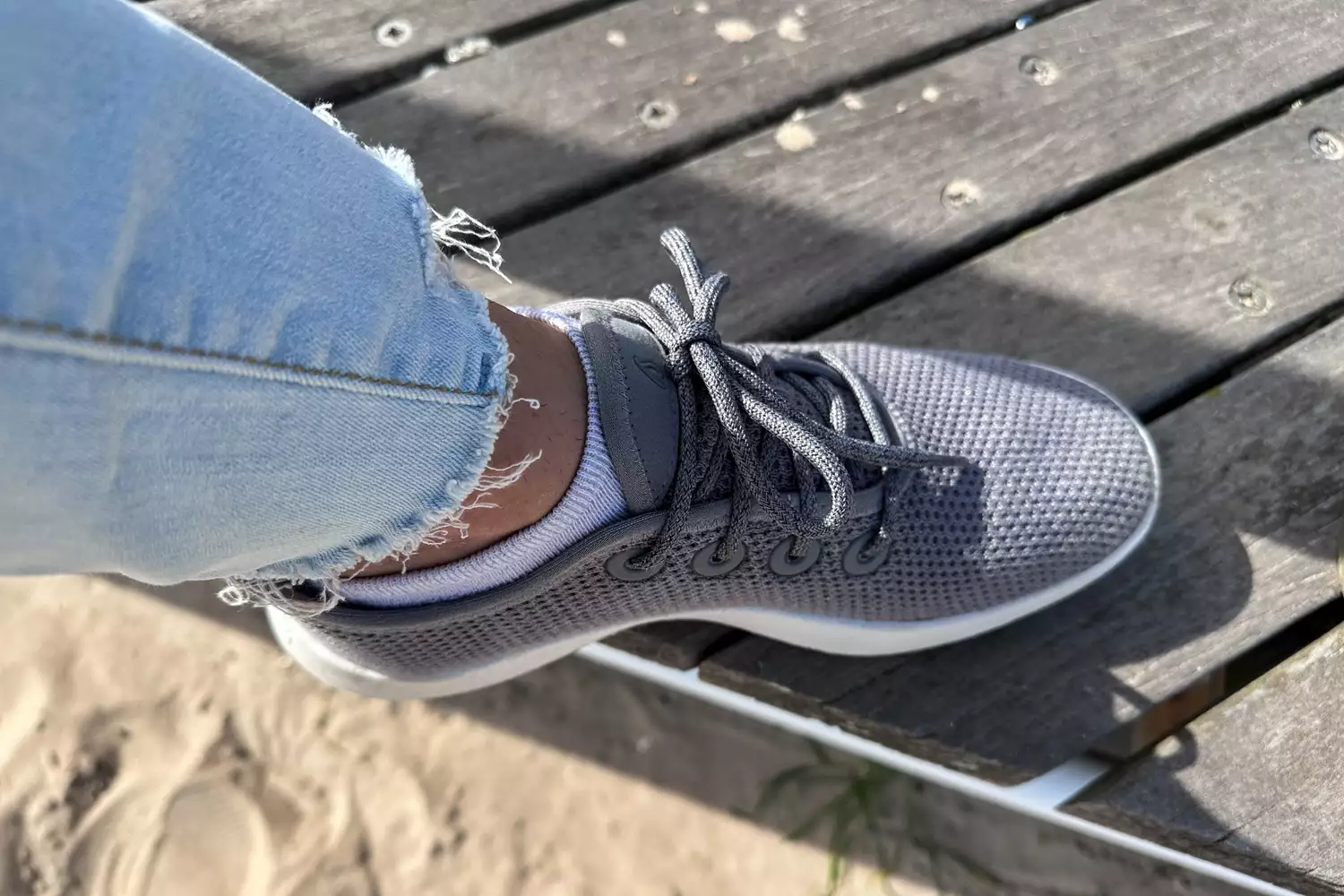 A person's foot in a gray Allbirds Tree Runner sneaker resting on a wooden deck.