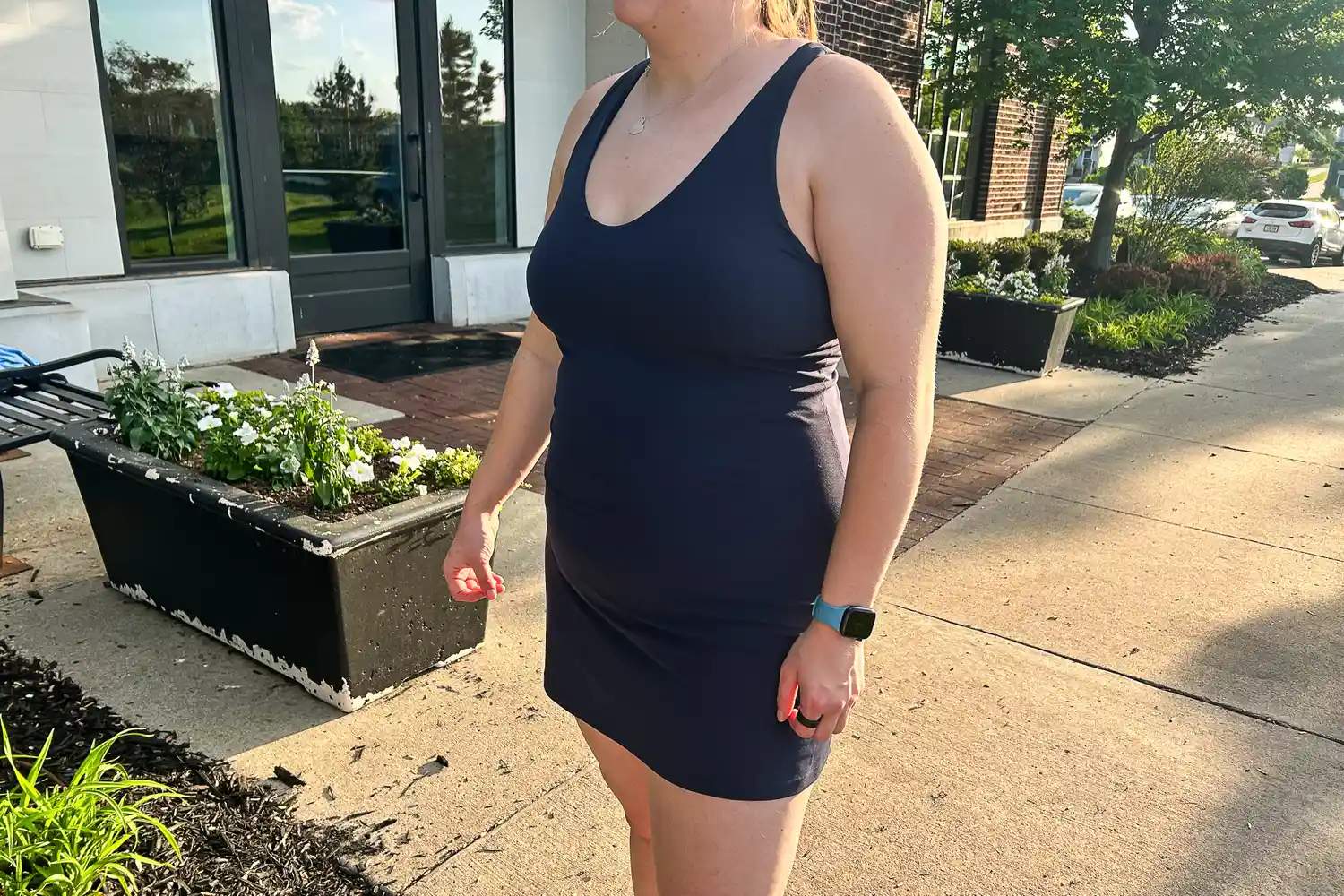 A woman wearing a navy blue Athleta Transcend Dress stands on a sidewalk.