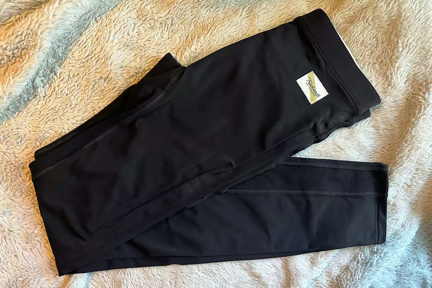 Dark Tracksmith turnover tights folded on a soft textured surface.