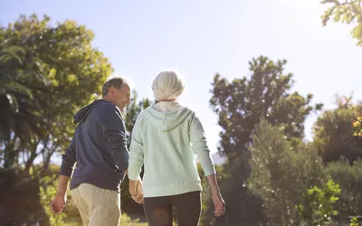 An older couple walking together in a sunny park to maintain mobility.