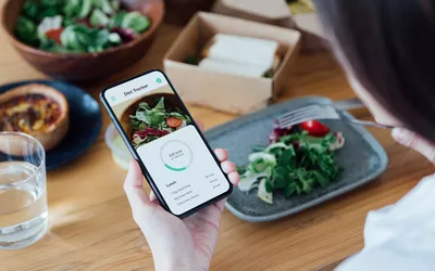 A person using a smartphone app to track the calories of a healthy salad at a table.