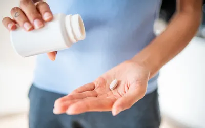 A person pouring a white pill from a bottle into their hand.