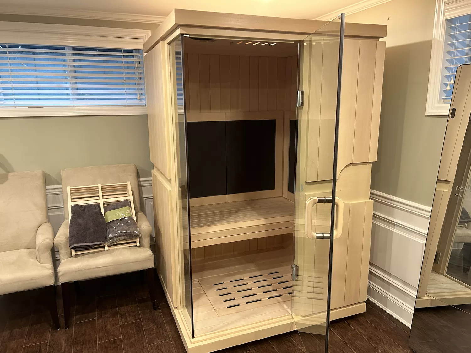 A spacious light-wood infrared sauna cabin with a full glass door in a modern living space.