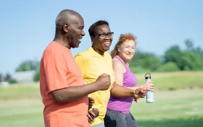 Three seniors walking together outdoors with water bottles.