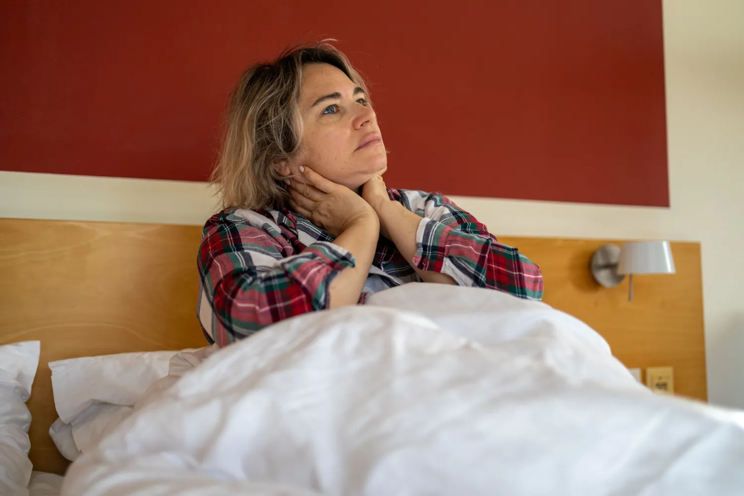 A person sitting up in bed, appearing to have difficulty sleeping or feeling fatigued.