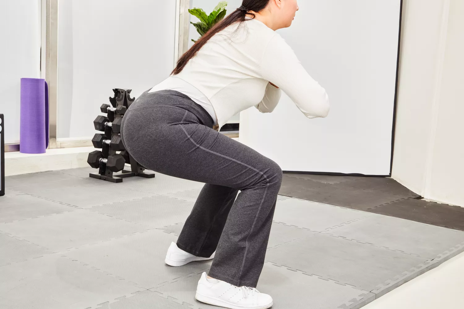 A woman performing a bodyweight squat in a home gym to test legging opacity and fit.