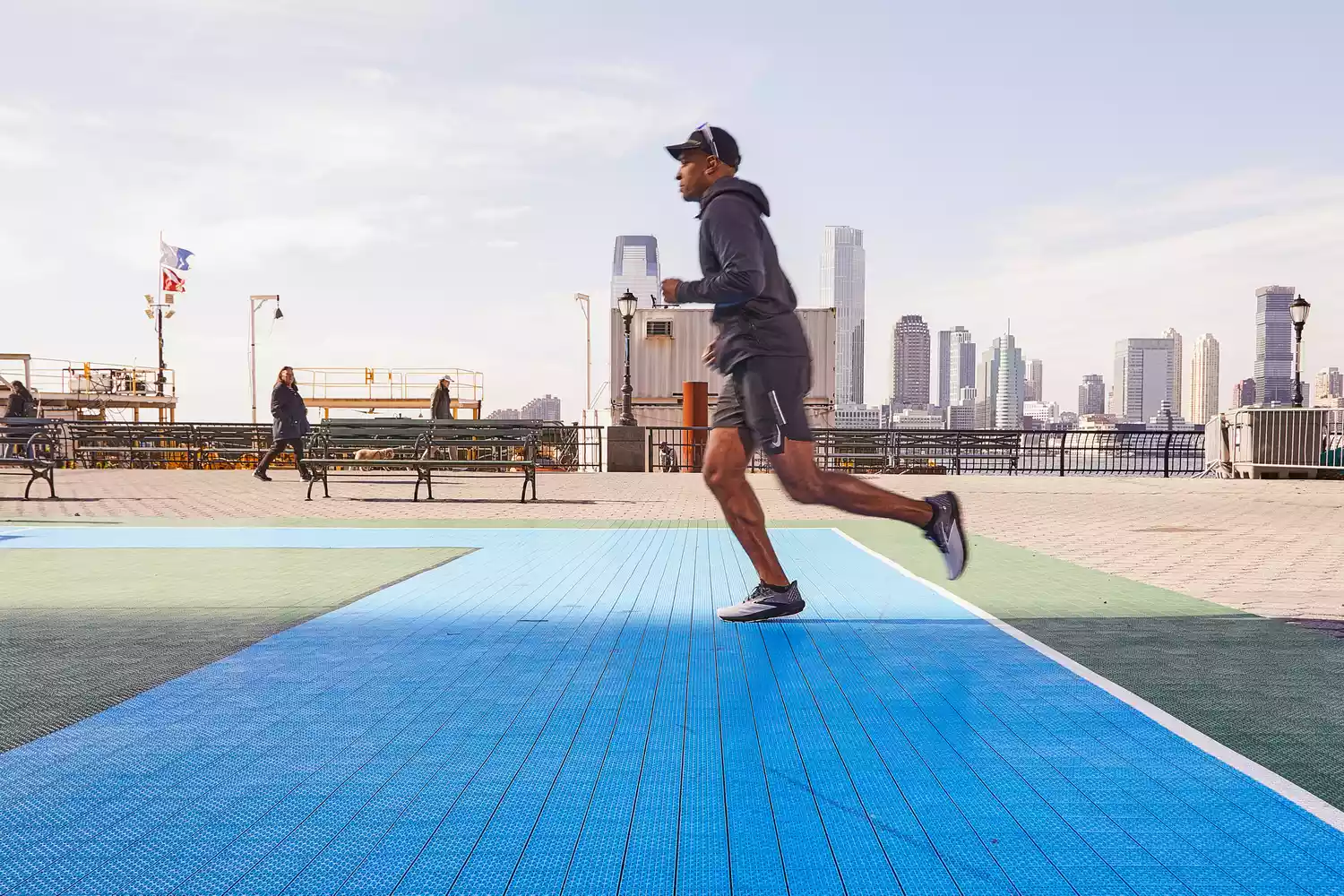 A man running on a blue outdoor track with a city skyline in the background.