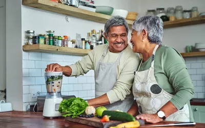 An older couple in a kitchen preparing a healthy vegetable smoothie together.
