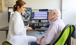 A doctor and an elderly patient discussing brain scan results on a computer monitor in a clinical office.