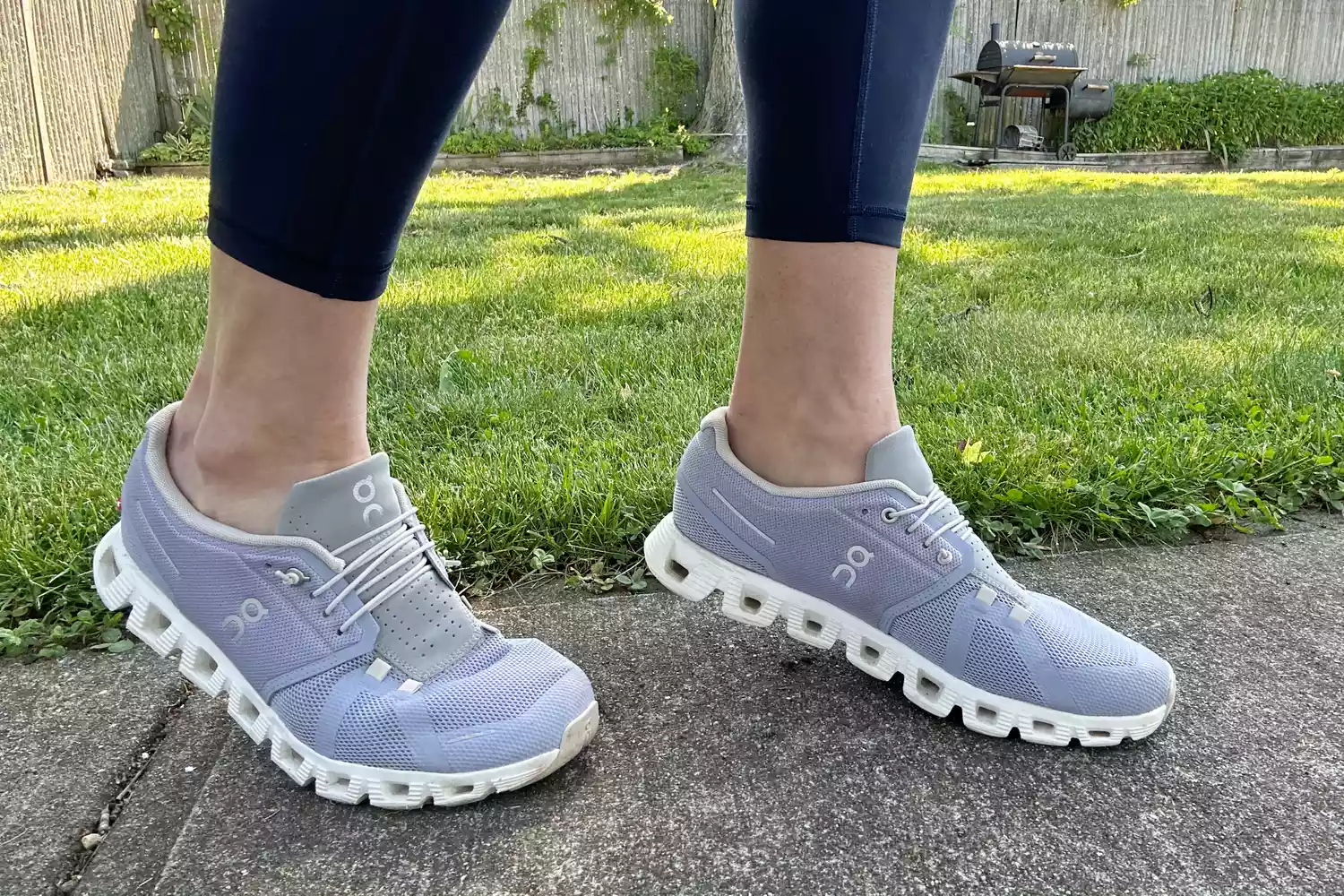 A person wearing light purple ON Cloud shoes standing in a backyard setting.