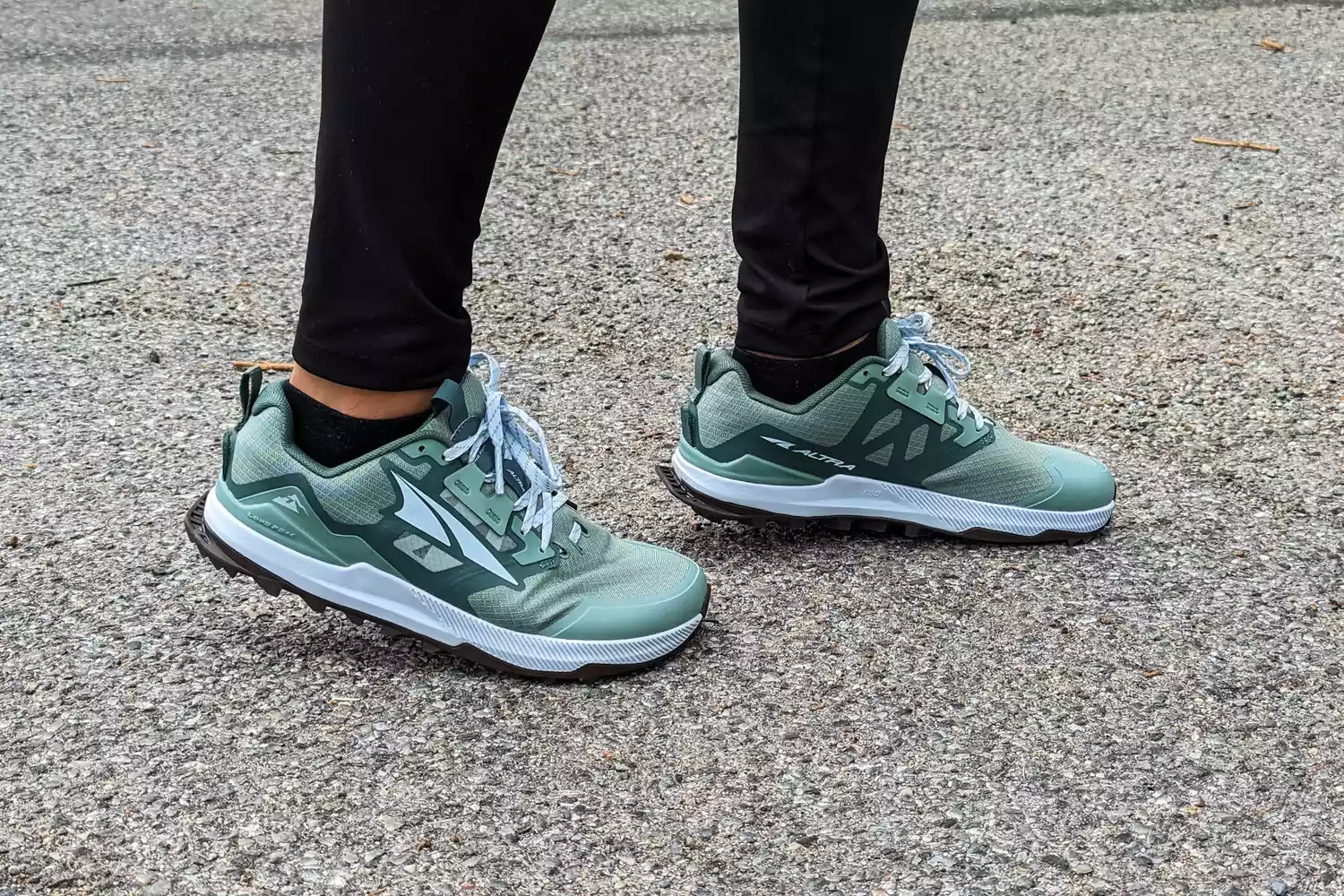 A person wearing Altra Lone Peak trail shoes standing on a gravel and paved surface.