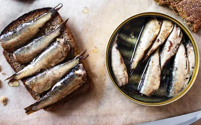 An open tin of sardines next to a slice of toast topped with whole sardines and oil.