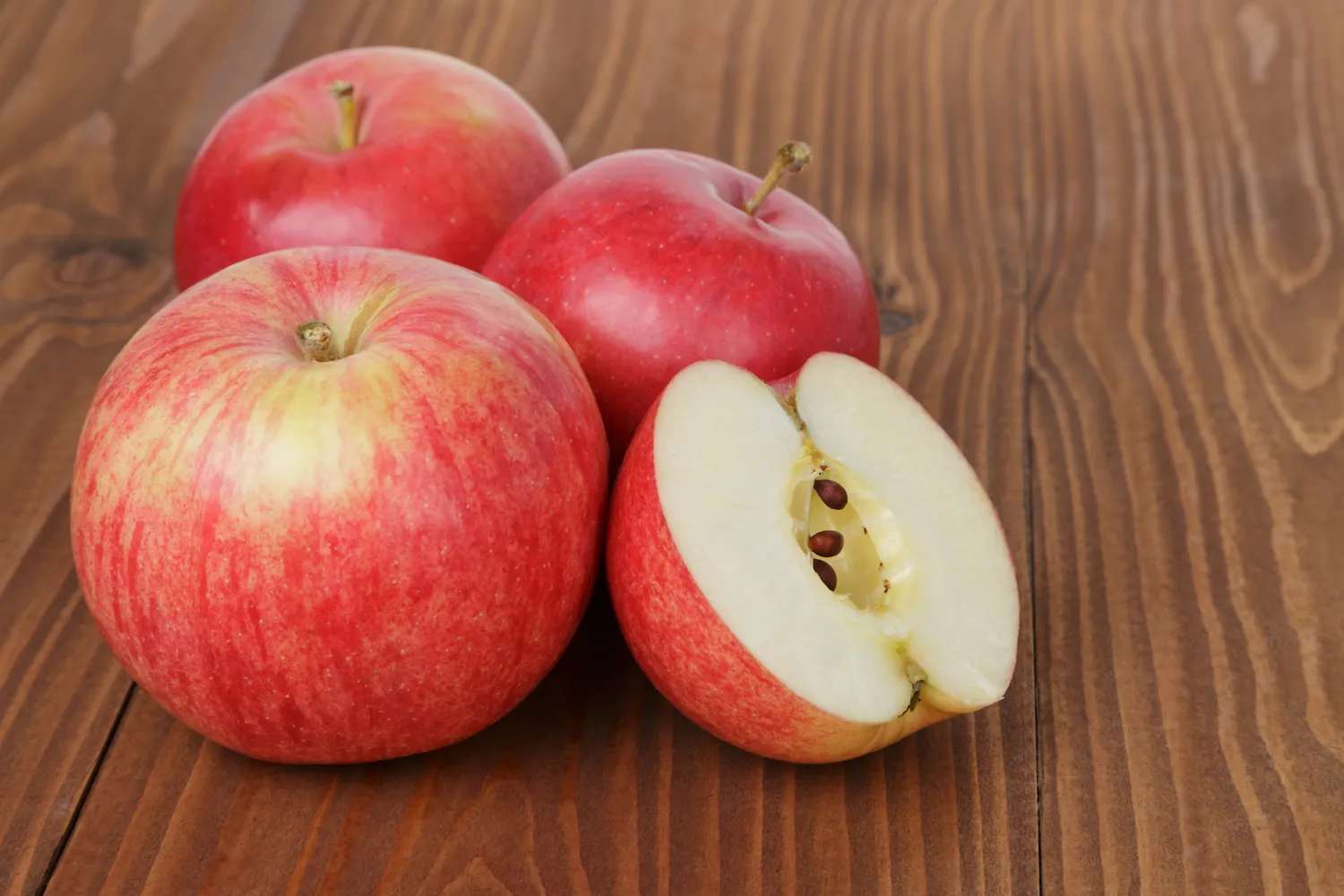 A close-up of a sliced red apple showing the core on a wooden surface.