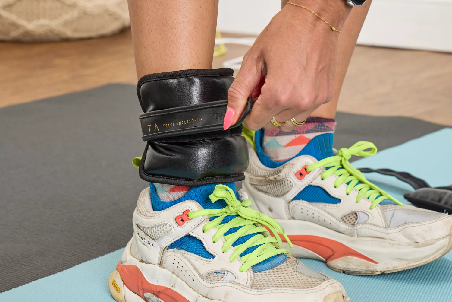 A person attaching a black leather Tracy Anderson ankle weight to their ankle.