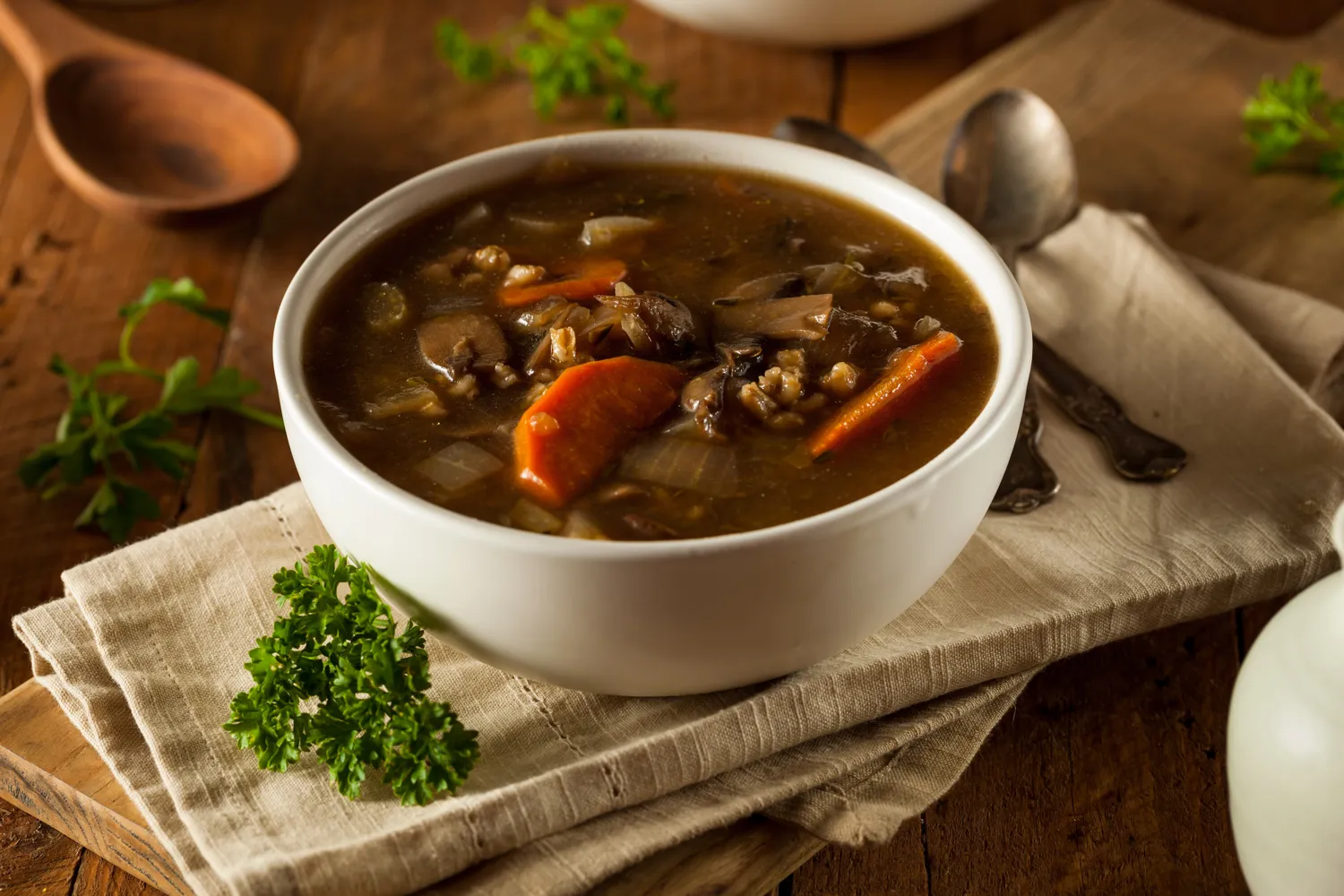 A bowl of mushroom barley soup served on a wooden table.