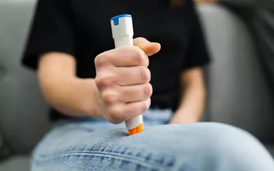 A person preparing a medical auto-injector against their thigh for emergency treatment.