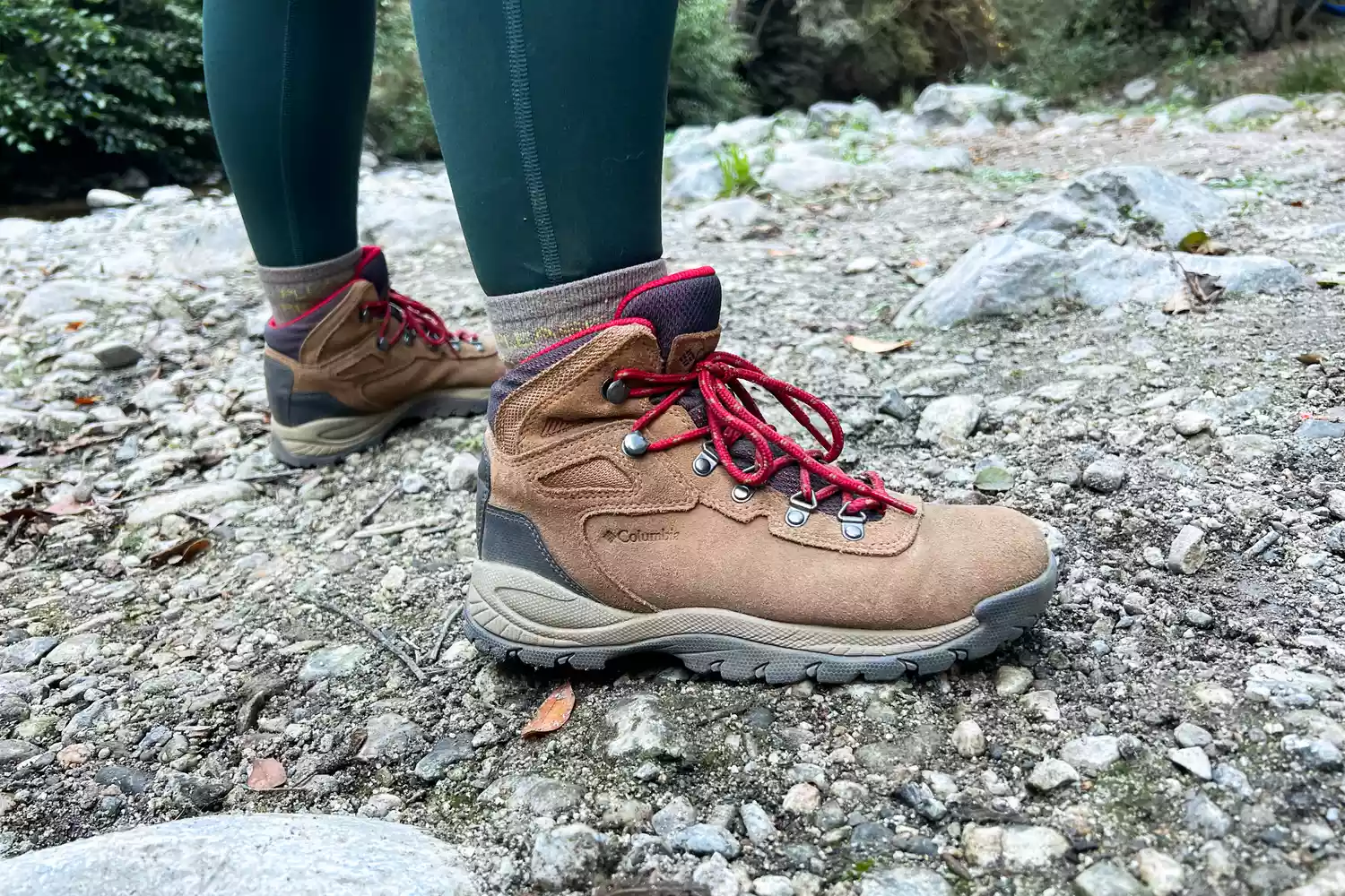 A hiker wearing Columbia Newton Ridge boots standing on a rocky mountain path.