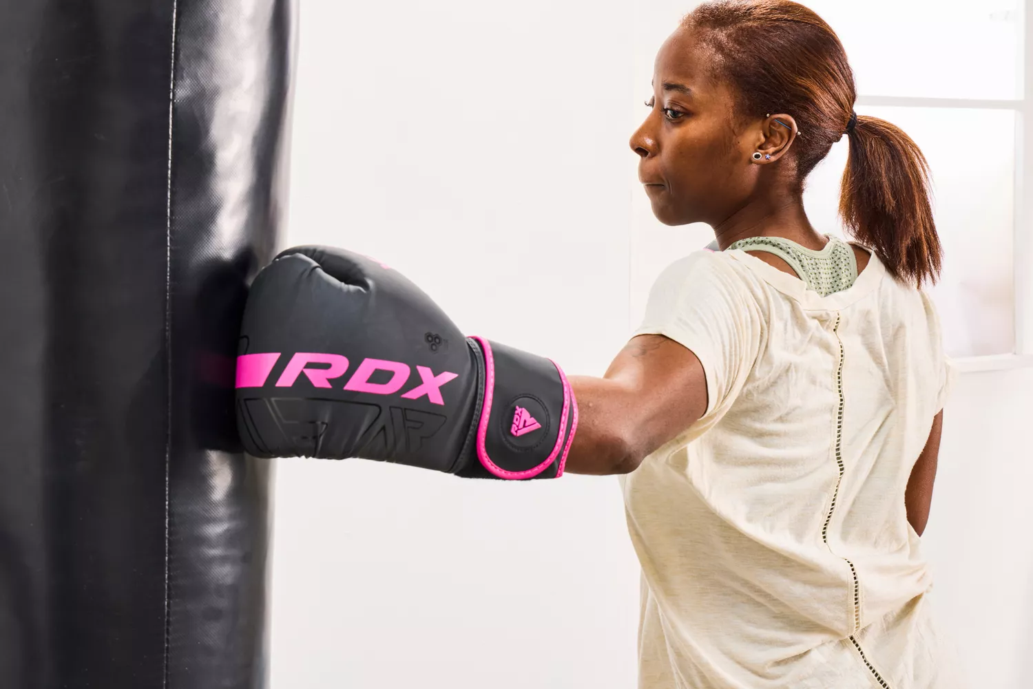 A woman wearing RDX gloves punching a heavy bag in a gym.
