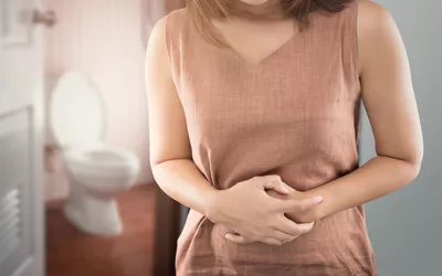 A woman in a pink top holding her stomach in a bathroom setting.