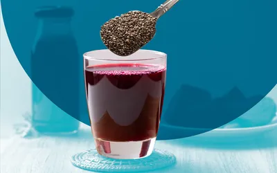 A glass of red juice with chia seeds being added, showing a healthy beverage preparation.